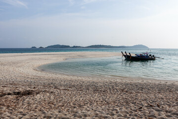 Obraz premium Long-tail boats anchored near Koh Adang beach. Sandy beach meets clear blue waters. Distant islands visible under a clear sky.