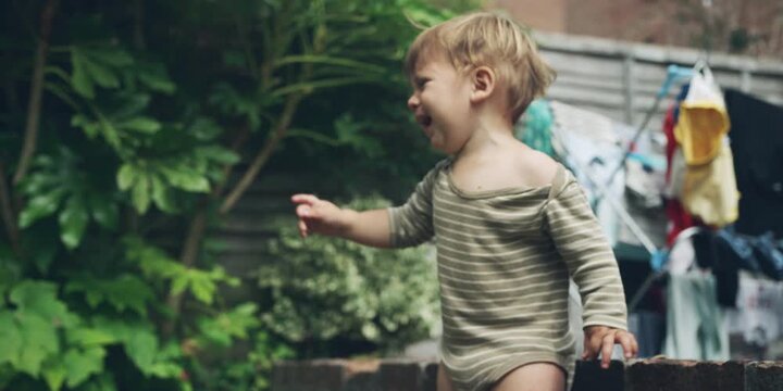 Toddler stands in a backyard, wearing a long-sleeved striped onesie.
