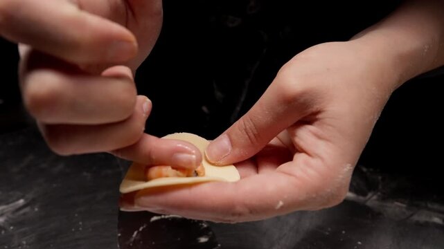 Closeup of hands carefully shaping and sealing small filled dumplings on a floured surface, highlighting delicate finger movements and detailed homemade cooking technique