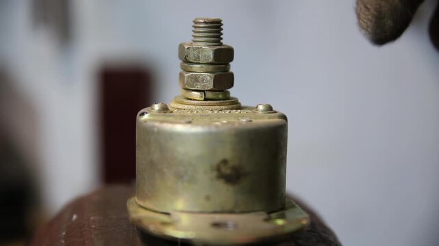 Hand in dirty work glove uses wrench to tighten nuts on threaded post of electrical component. Component solenoid or relay. Work suggests repair or assembly indoors.