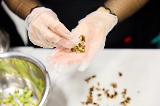 Woman in Gloves Shelling Fresh Pistachios over Bowl