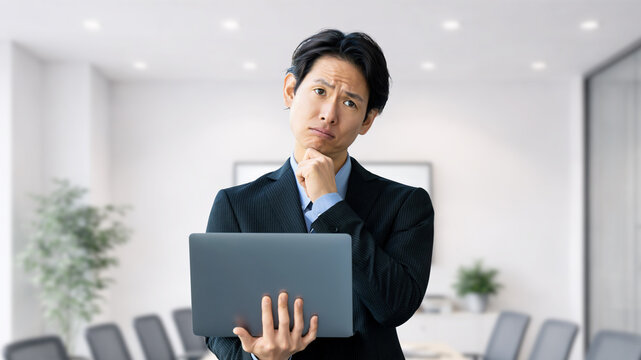 ノートパソコンを持ち考える男性ビジネスパーソン, Businessman thinking while holding a laptop