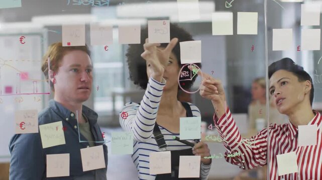 3 coworkers clustering at glass wall, center reaching up moving sticky notes for product plan