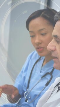 Vertical video: Nurse tapping tablet to review patient vitals in medical consult, HUD showing scans