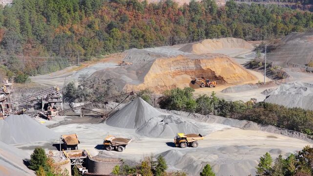 Aerial wide overview of quarry operations and haul trucks with front loader digging away