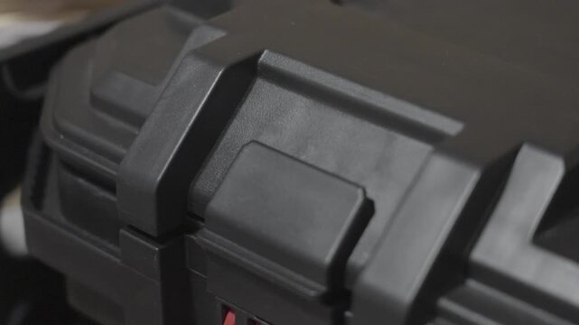 A hinge in the open position on a black tool storage bin.