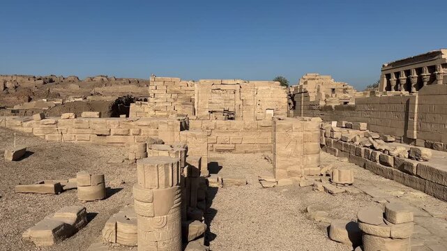 Wide panoramic shot of the archaeological ruins and scattered stone blocks at the Dendera Temple complex in Egypt with the main temple in the background