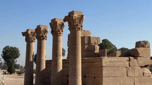 Wide shot of four ancient stone columns with ornate capitals standing on a stone platform within the archaeological site of Dendera Temple in Egypt