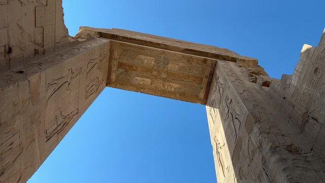 Low angle cinematic shot looking up at the decorated ceiling and reliefs of the monumental ancient stone gateway known as propylon at the Temple of Hathor in Dendera Egypt
