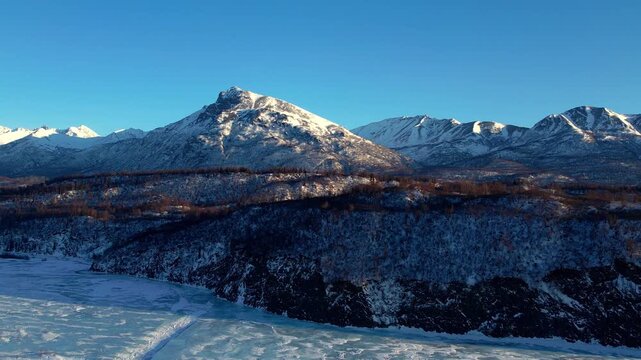Drone pullback with counter-clockwise rotation above frozen Matanuska River Valley near Palmer, AK. Snow-covered peaks, boreal forest, and blue winter sky. DJI Air 2S 4K 60fps.