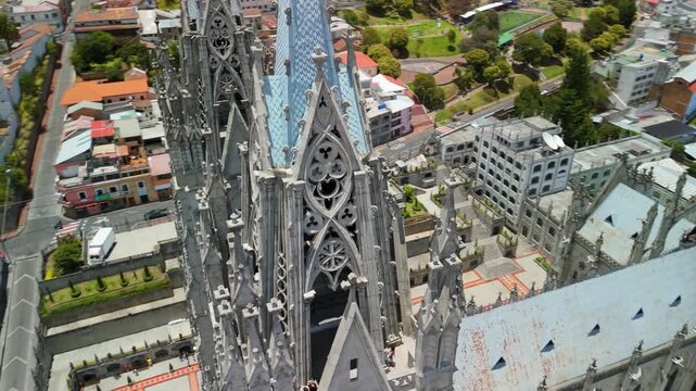 Drone orbits at high angle extremely close to Gothic stone spires and tracery of Basilica del Voto Nacional in Quito with city rooftops far below
