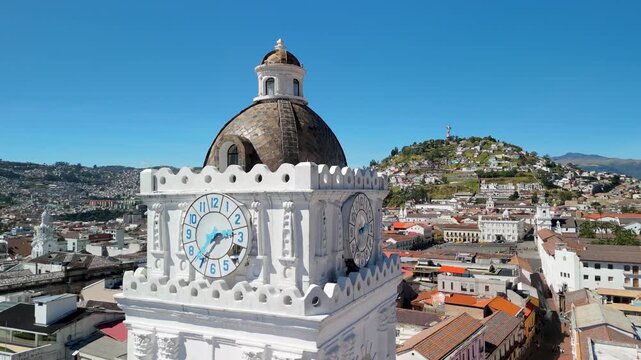 Aerial parallax orbits La Merced Basilica white square clock tower with blue numerals brown tiled dome against Quito cityscape