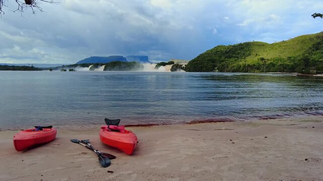 Beach at Canaima Lagoon with kayaks on the shore, El Hacha, Golondrina, Wadaima, and Ucaima waterfalls, and the Nonoy, Kuravaina, and Topochi tepuis, in the background Venezuela.