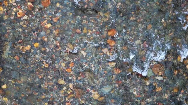 Drone top down shot of crystal clear river water flowing over vibrant stones and pebbles in natural freshwater stream in Spain. Scenic nature background for travel and summer themes.
