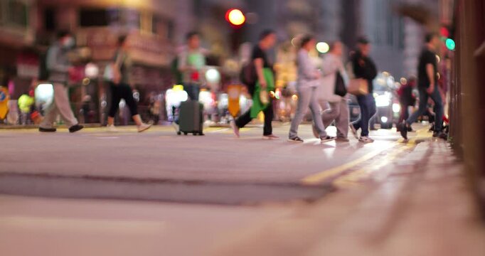 People walk on pedestrian crossing at Hong Kong Island city street, slow motion shot in evening with tilt-shift effect. Faces of passers by is blurred, focus on legs and bottom of frame blurred too.