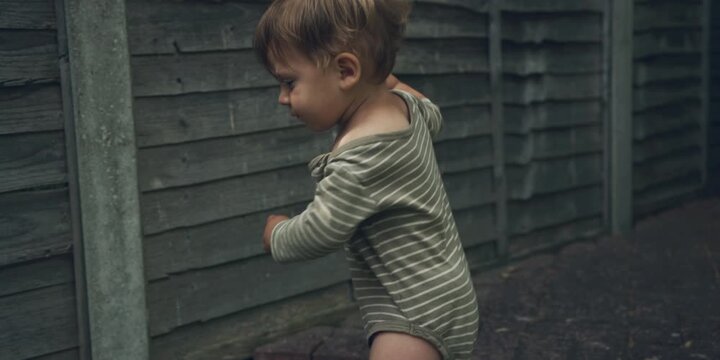 Young child walks in a yard, wearing a green and white striped shirt