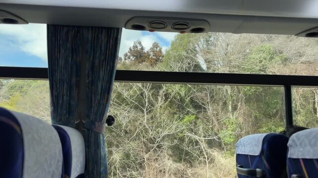 Inside view of a tour bus window with a scenic mountain landscape and winding road during a spring trip (4K)