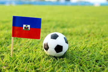 Fototapeta premium Haiti national flag beside a classic soccer ball on a green football stadium field symbolizing international competition national pride Caribbean football spirit and match anticipation.