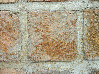 A wall made of about 3 old square bricks of varying shades of brown with jagged edges, held together with grey cement.