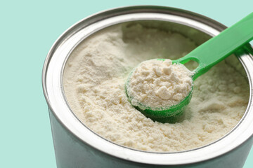 Naklejka premium Jar of powdered baby milk formula with measuring scoop on turquoise background, closeup