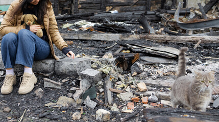 a person sitting amidst the charred remains of a destroyed building. Clad in a tan puffer jacket...