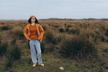 Woman lifestyle concept with a young woman wearing autumn clothes standing in a field. She looks...