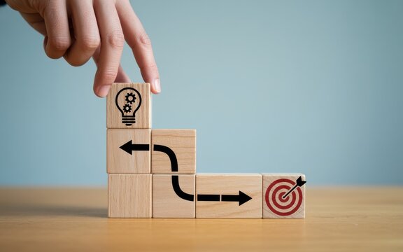 Hand placing wooden block with lightbulb icon on a path leading to a target for business strategy concept