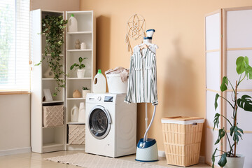 Interior of laundry room with folding screen, shelving unit, modern steamer, washing machine and...