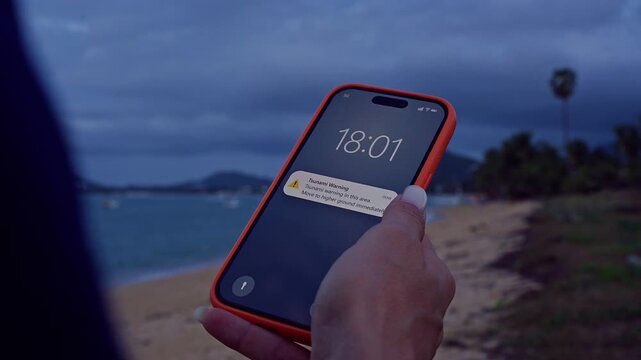 Woman Holding Smartphone on Stormy Beach Receiving Tsunami Warning Alert Notification With Dark Clouds Over Ocean Cinematic Close Up Zoom Shot