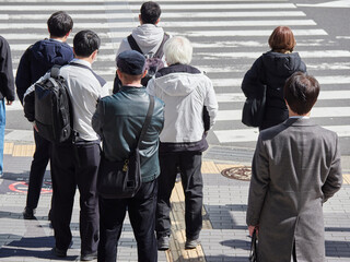 ハイアングルで撮影した春の昼の都市の交差点の横断歩道で信号待ちのビジネスマンの姿