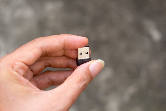 Close-up portrait photo of a hand holding a black 2.4GHz USB wireless dongle. Technology device used for wireless connectivity with computer peripherals and gadgets.