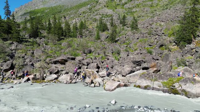 aerial drone footage 4K, tourists make their way along a mountain river on boulders