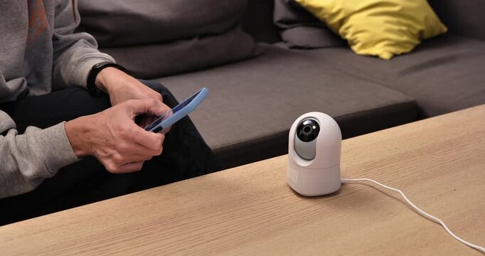 Smart Home Control: A person uses smartphone to monitor a smart home security camera. The scene illustrates convenience and control over domestic surveillance from smartphone.