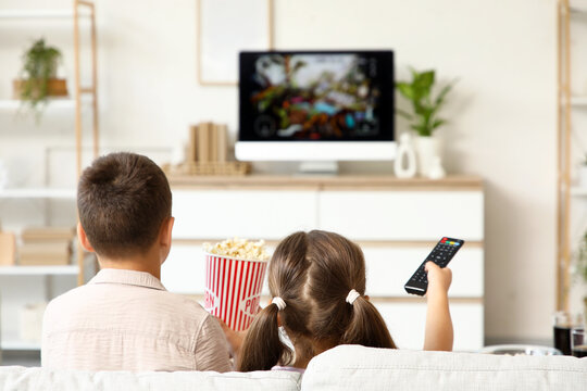 Cute friends with popcorn and TV remote control watching cartoons on sofa at home, back view