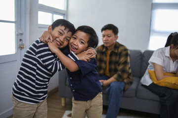 Obraz premium Two Happy Boys Hugging and Smiling in Cozy Living Room While Their Parents Arguing in Background
