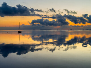 Small boat with mast reflected in calm water during sunrise over Mar Menor lagoon in Los Alcázares, Spain. Peaceful Mediterranean seascape with mirror reflection. © Elena Sistaliuk