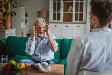 Senior man having headache during healthcare home visit