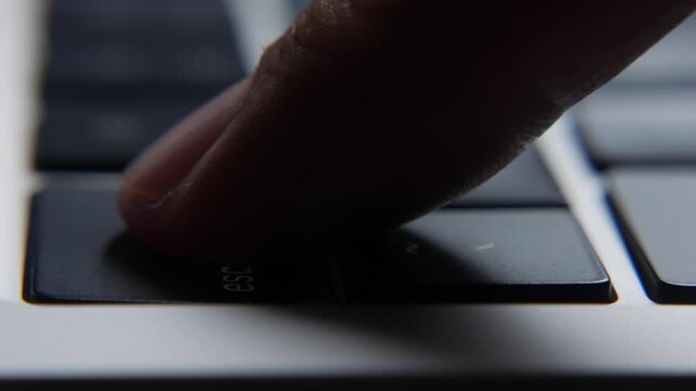 Finger repeatedly pressing the Esc key on a laptop keyboard in a close view showing quick repeated command input during computer use. System error, software glitch.