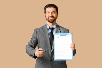 Young happy male real estate agent with house rental agreement and pen on beige background