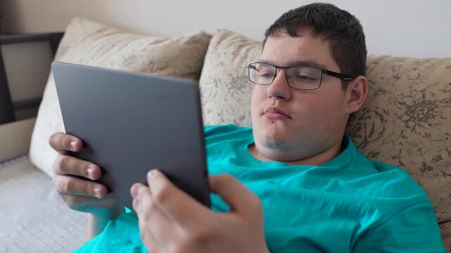 A teenager in glasses looks intently at a tablet screen, focused on the display.