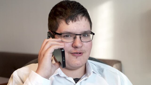 Smiling teenage boy talking by smartphone on grey background.