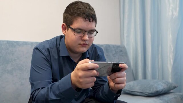 A teenager plays on a smartphone while sitting at home, focused on the screen.