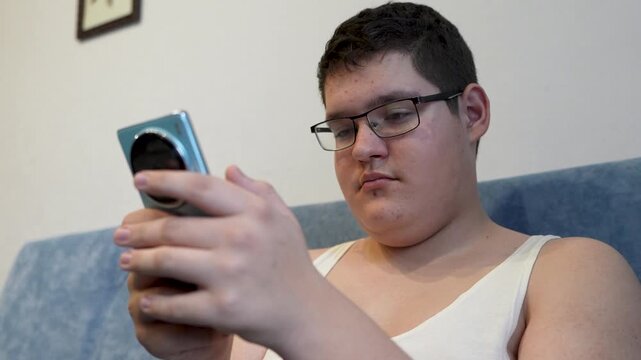 Caucasian teen boy texting on smartphone at home. A focused teenager fiddles with his smartphone while browsing messages or content on the Internet.
