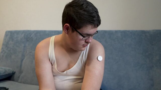 A young man attaches a glucose sensor to his arm for blood sugar monitoring, representing diabetes care and management.