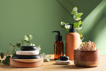 Bottles of cosmetic products, spa stones and bath supplies on wooden table near green wall © Pixel-Shot