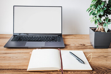 Minimal freelancer workspace with laptop mockup screen, open notebook and indoor plant on wooden desk. Productivity, remote work and online business concept with copy space
