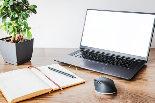 Modern home office workspace with laptop mockup screen, open notebook with pen, computer mouse and green houseplant on wooden desk. Remote work, freelancer planning and productivity concept