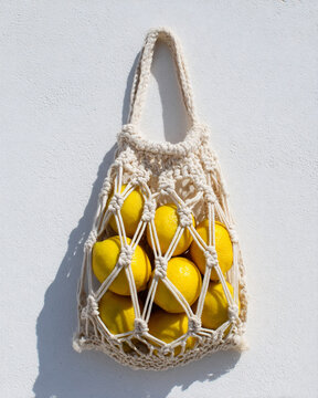 Displayed macrame bag with lemons hanging against a white wall during daytime
