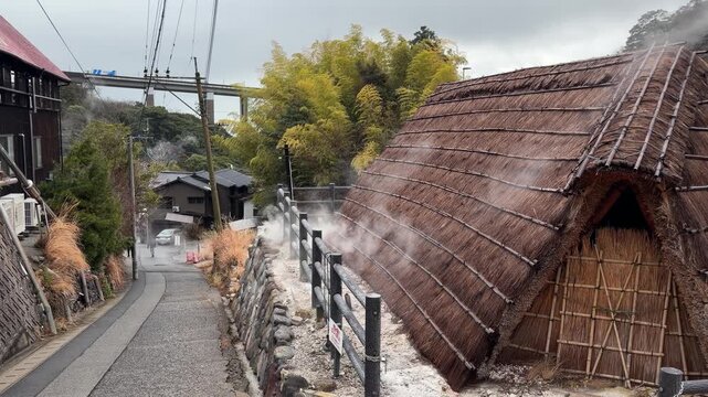 Traditional Japanese onsen landscape with volcanic steam and thatched huts at Myoban Jigoku (4K)
