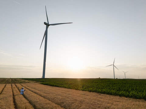 Female farmer with digital tablet near wind turbines in aerial rural field